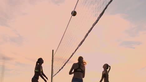 Las-Chicas-Del-Partido-De-Voleibol-De-Playa-Golpean-La-Pelota-En-Cámara-Lenta-Al-Atardecer-En-La-Arena.